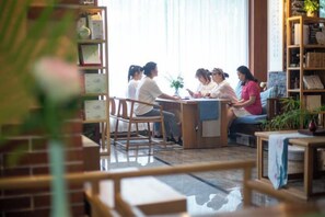 Un groupe de personnes est assis autour d’une table dans une pièce où se trouvent une bibliothèque et une plante.