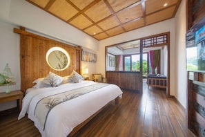 Ein Schlafzimmer mit einem großen Bett, Holzboden und Blick ins Freie.