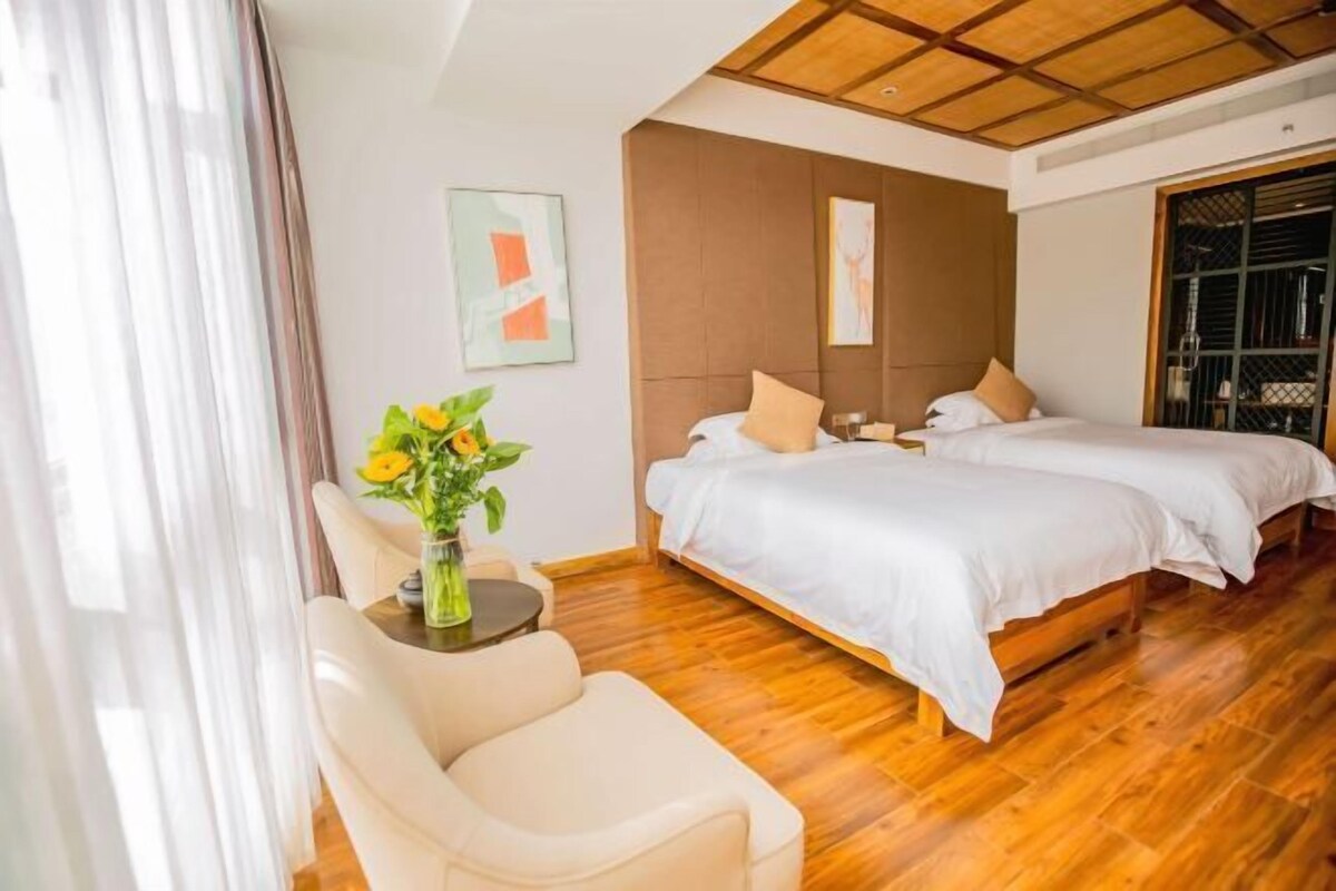 Une chambre d’hôtel avec deux lits, un plancher en bois, une chaise, une table ornée d’un vase de fleurs et des œuvres d’art accrochées aux murs.