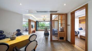Una habitación de hotel moderna con suelo de madera, una zona de comedor con mesa y sillas, vistas a través de un ventanal grande y una puerta corredera japonesa tradicional.
