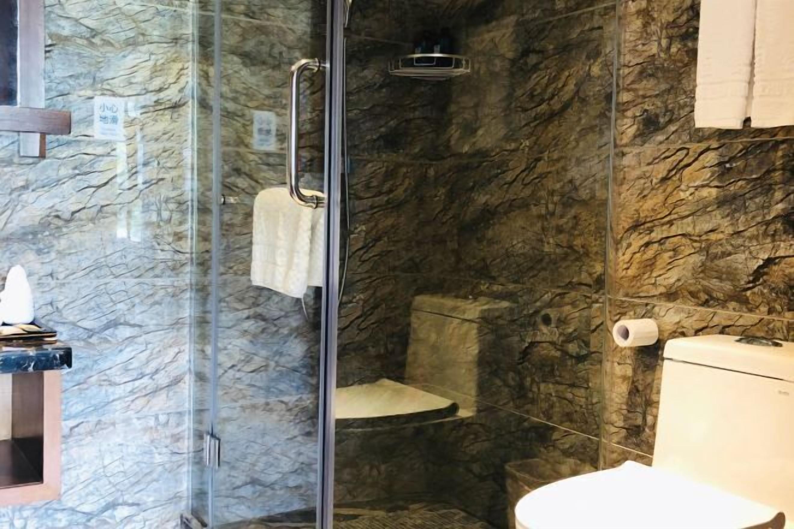 Un baño con ducha envuelta en vidrio, inodoro y pared de mármol.