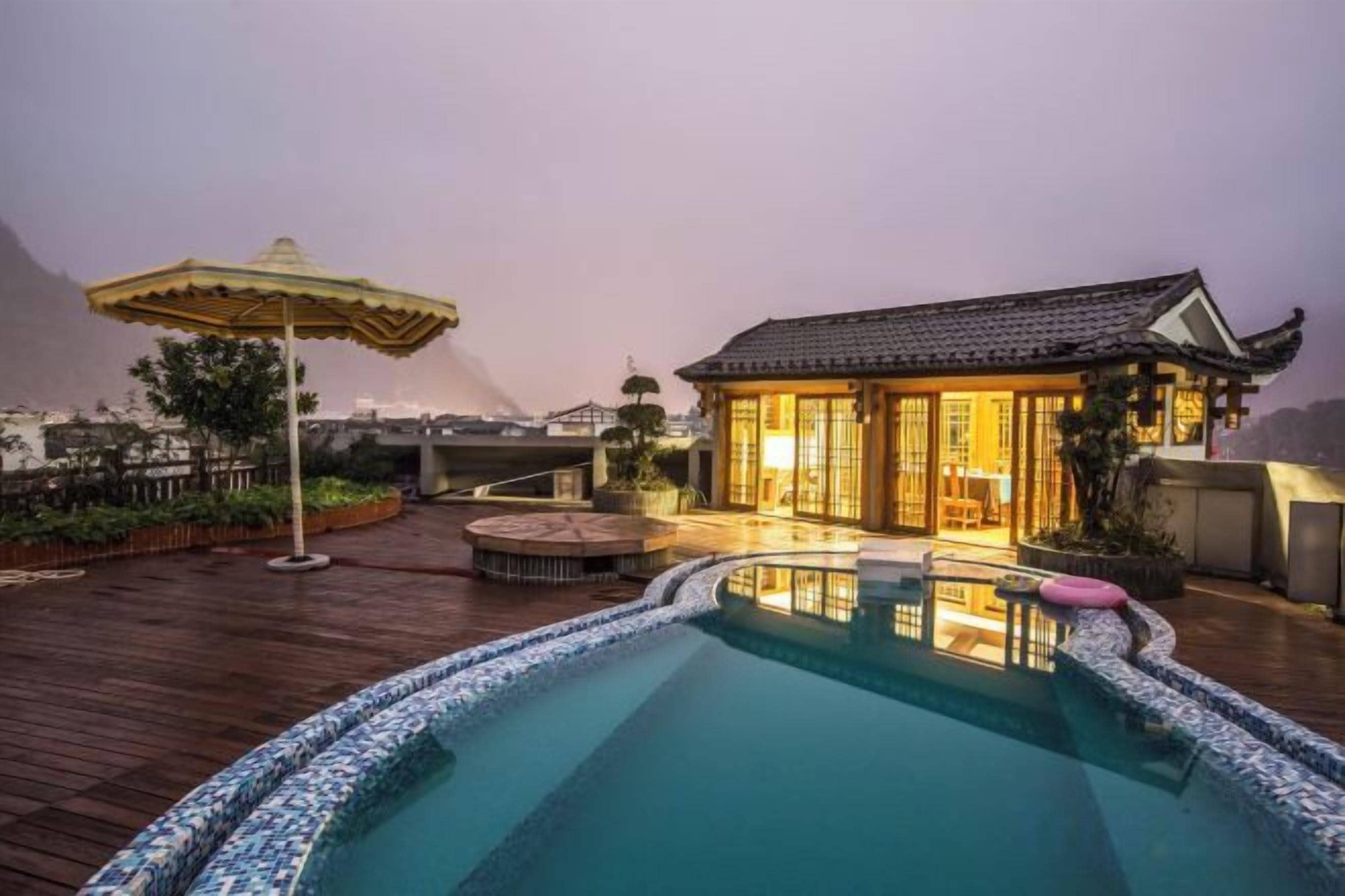 A rooftop pool area with a traditional building, a wooden deck, and an umbrella.