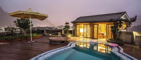 A rooftop pool area with a traditional building, a wooden deck, and an umbrella.