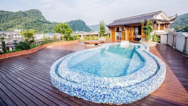 A rooftop pool with mosaic tiles, surrounded by wooden decking, and a traditional building with a tiled roof. - Baofeng Homestay (Zhangjiajie National Forest Park) (Zhangjiajie)