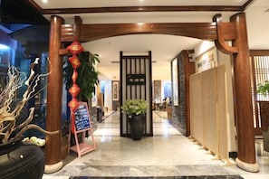 Un vestíbulo de hotel con una recepción, una planta en maceta grande y decoración tradicional.