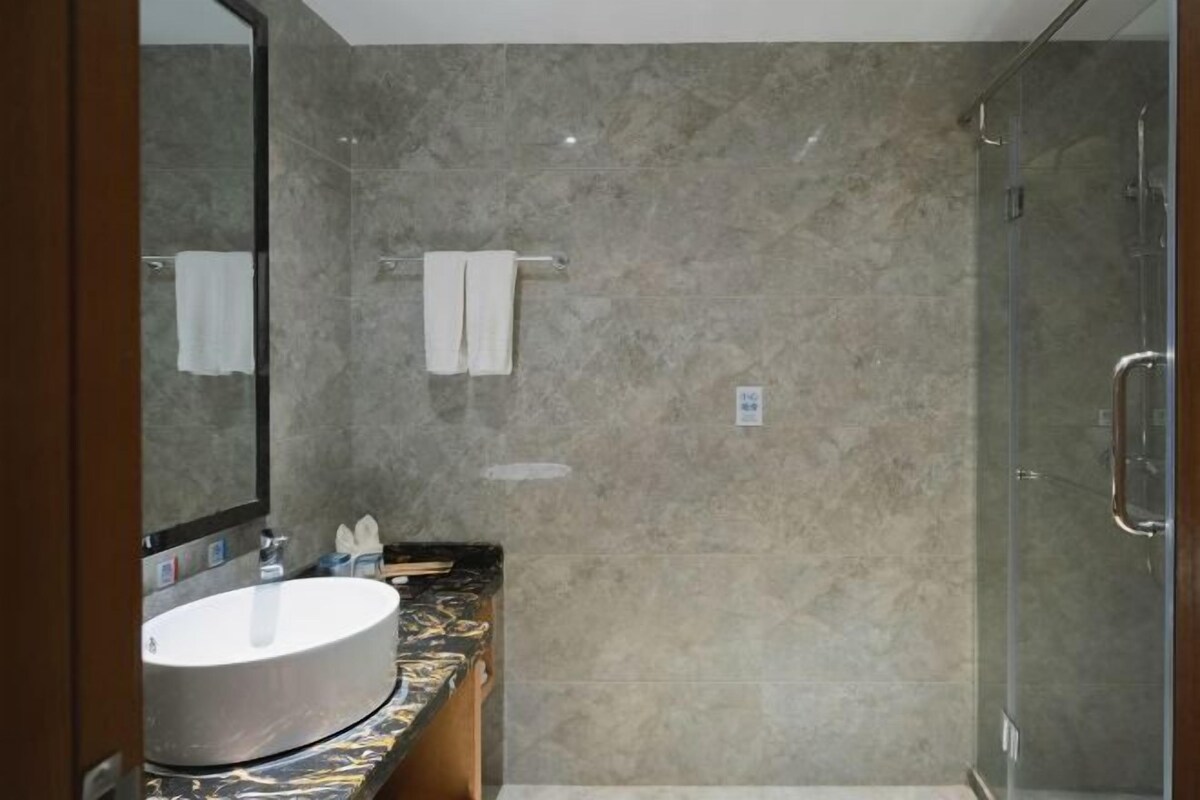 Une salle de bain dotée d’un grand miroir, d’un lavabo rond, d’une cabine de douche en verre et de murs en marbre.