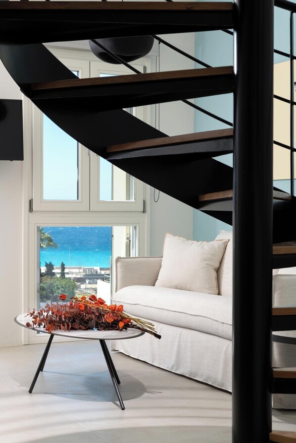 A modern living room with a white sofa, a glass coffee table with a floral arrangement, and a view of the ocean through large windows.
