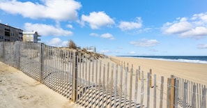 Une plage avec une clôture en bois, une plage de sable et des bâtiments en arrière-plan.