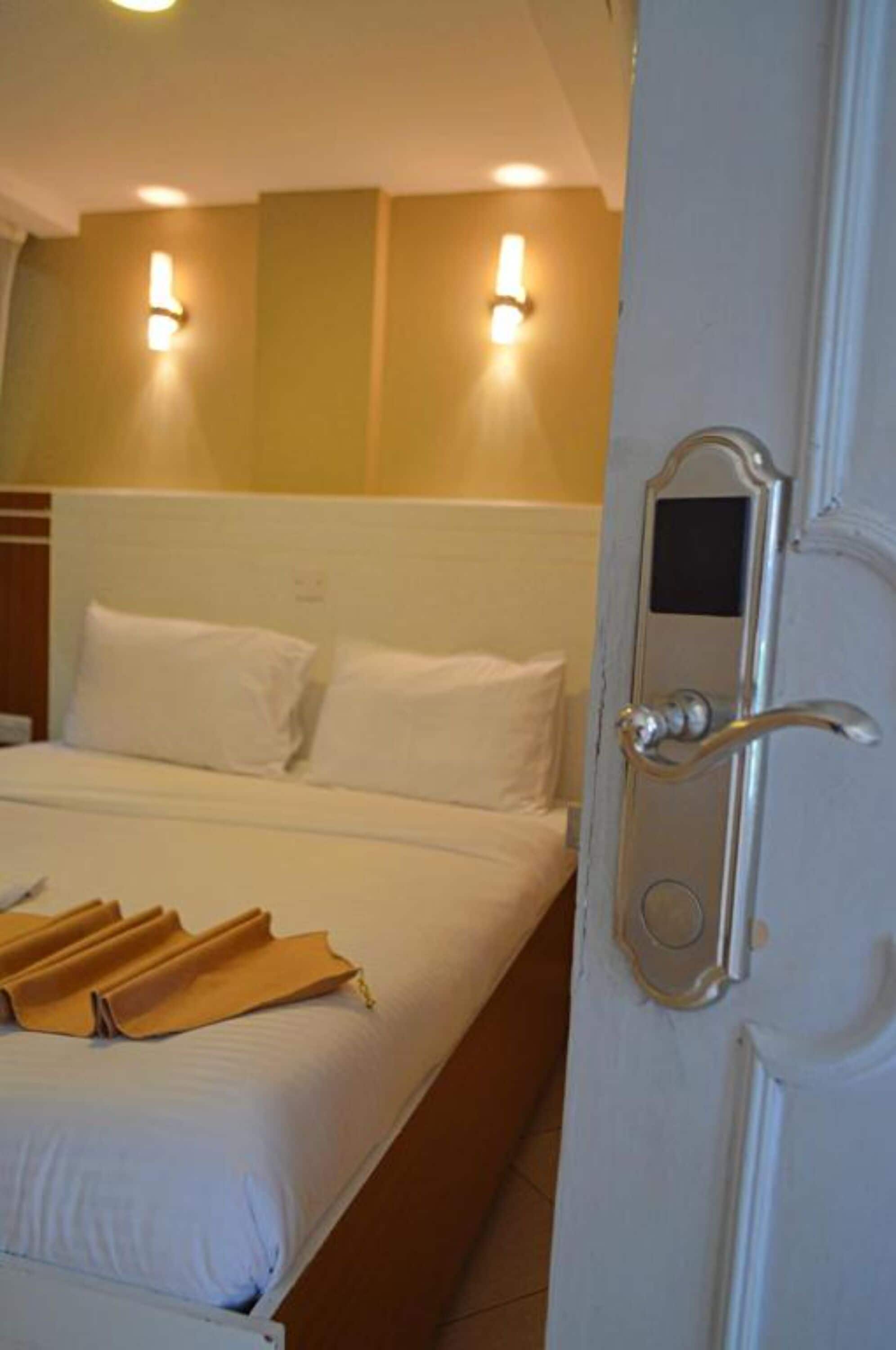 A hotel room with a bed, white linens, a door with a mirror, and wall-mounted lights.