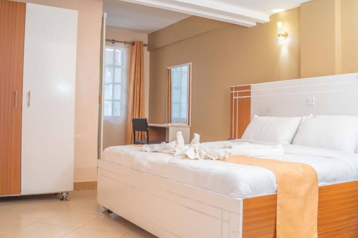 A hotel room with a bed, a desk, a chair, and a wardrobe.