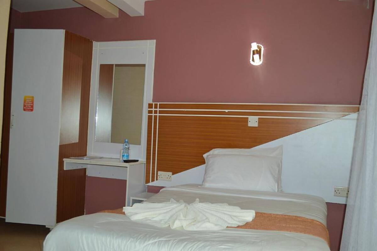 A hotel room with a bed, a bedside table, a mirror, and a door.