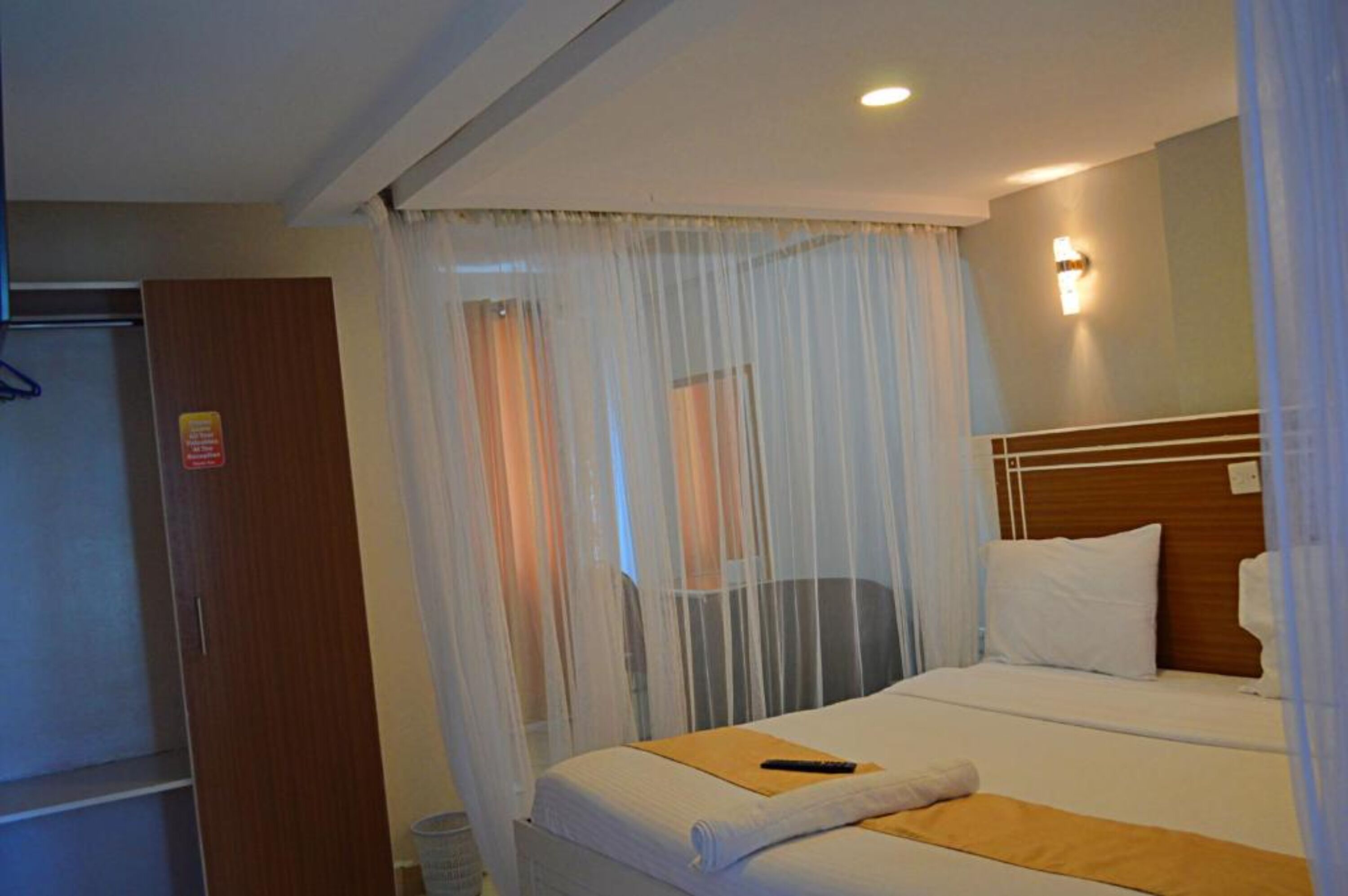 Une chambre d’hôtel avec un lit, une tête de lit en bois, une table de chevet, une télécommande et une moustiquaire.