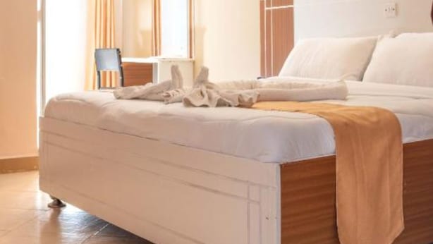 A bedroom with a bed, a bedside table, a mirror, and a window with curtains. - Montana Resort Naivasha (Naivasha)
