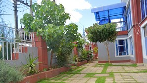 A courtyard with a paved walkway, a tree, and a building with a blue roof. - Montana Resort Naivasha (Naivasha)
