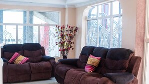 A living room with two brown sofas, a vase with flowers, and large windows with a view of buildings. - Montana Resort Naivasha (Naivasha)