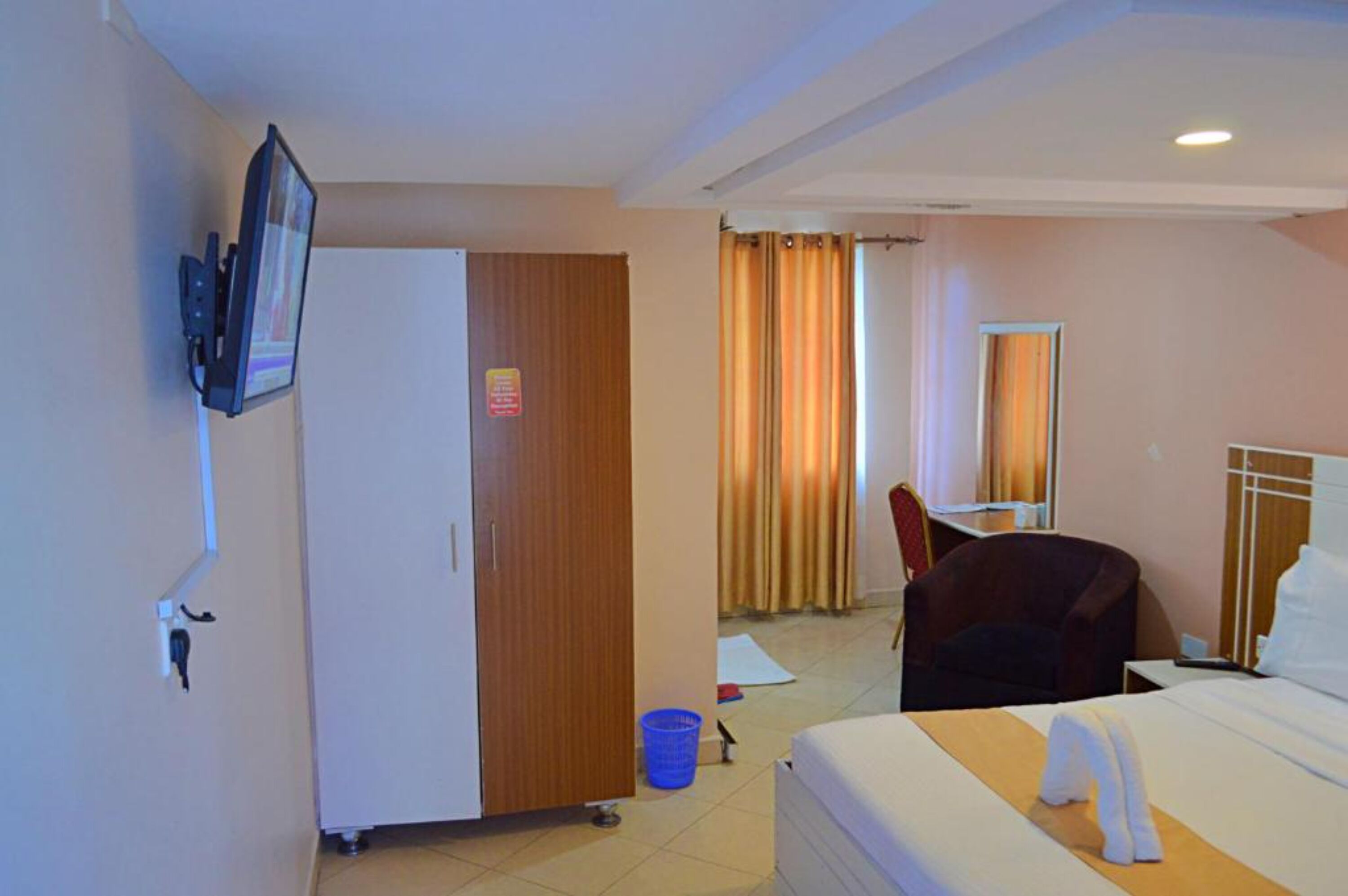 A hotel room with a bed, a desk, a chair, a wardrobe, a television, and a bathroom with a shower curtain.