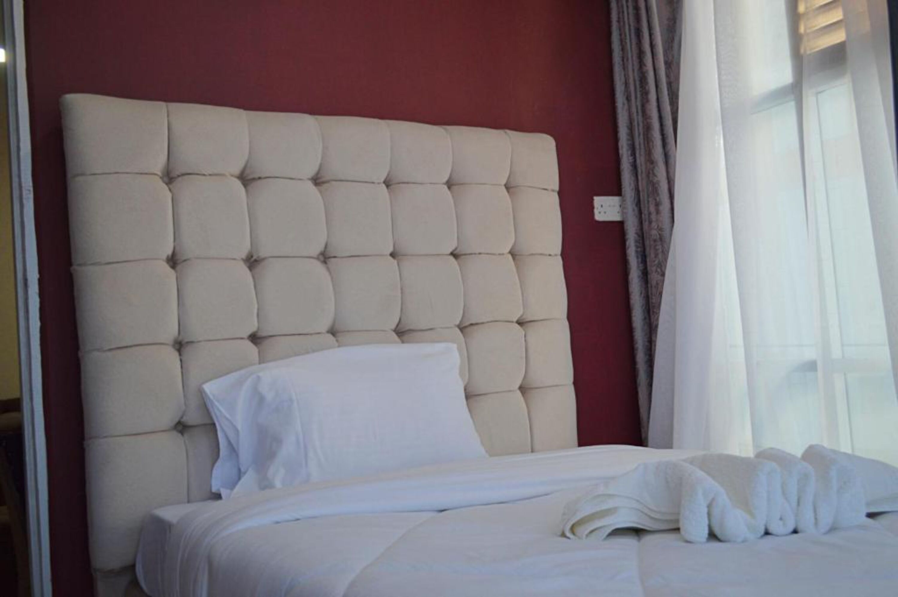 A neatly made bed with a tufted headboard, white bedding, and a window with curtains.
