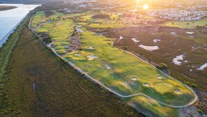 An aerial view of a golf course with multiple holes, a water body to the left, and a residential area in the background. - Los Albatros - Haraganes Beach HAHB174P170 (Isla Canela)