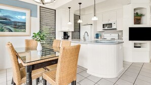 A modern kitchen with white cabinetry, a central island, and pendant lighting. - Tranquil Retreat w/Split AC - Kiahuna 2052 (KOLOA)