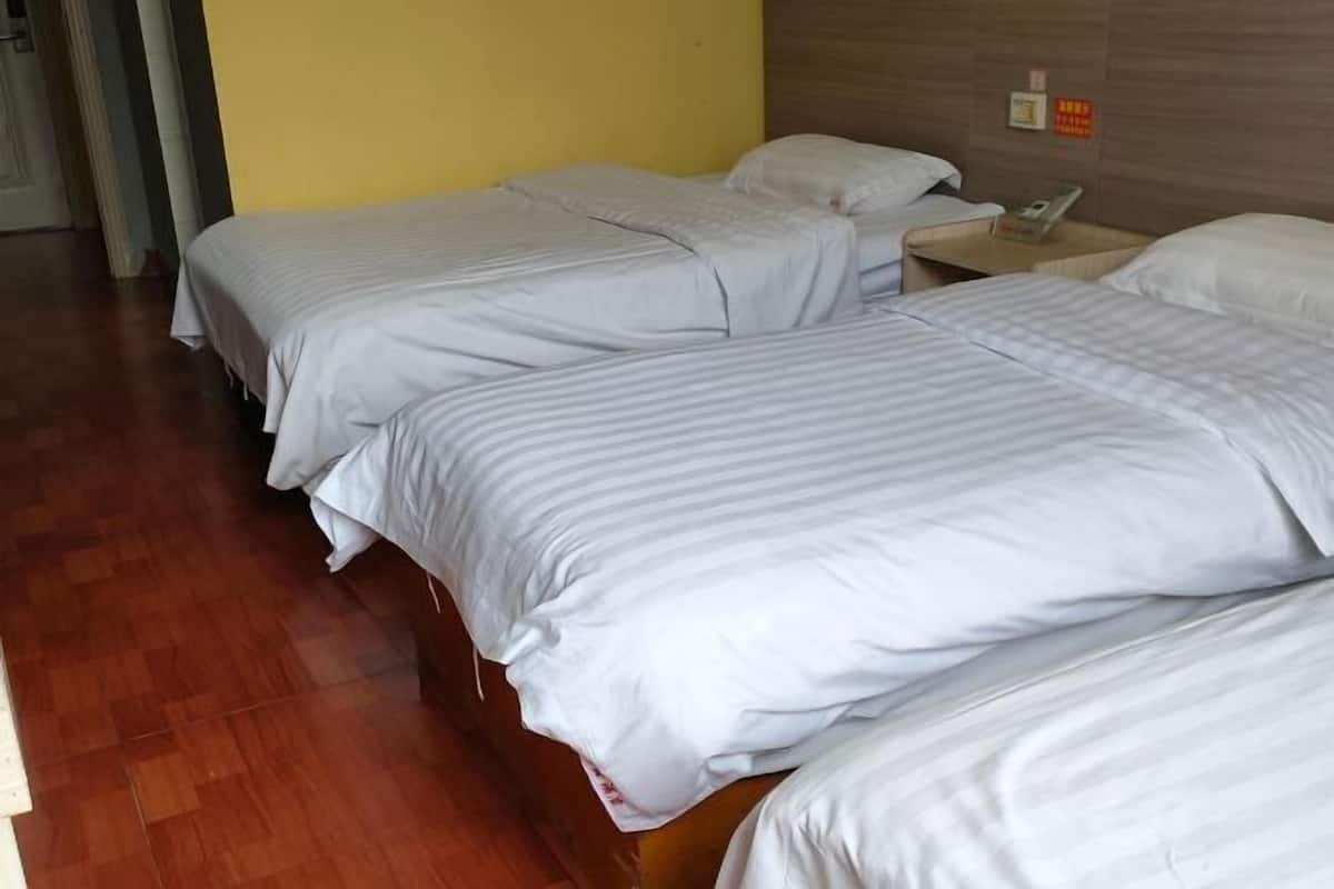 A hotel room with two single beds, wooden flooring, and a yellow wall.