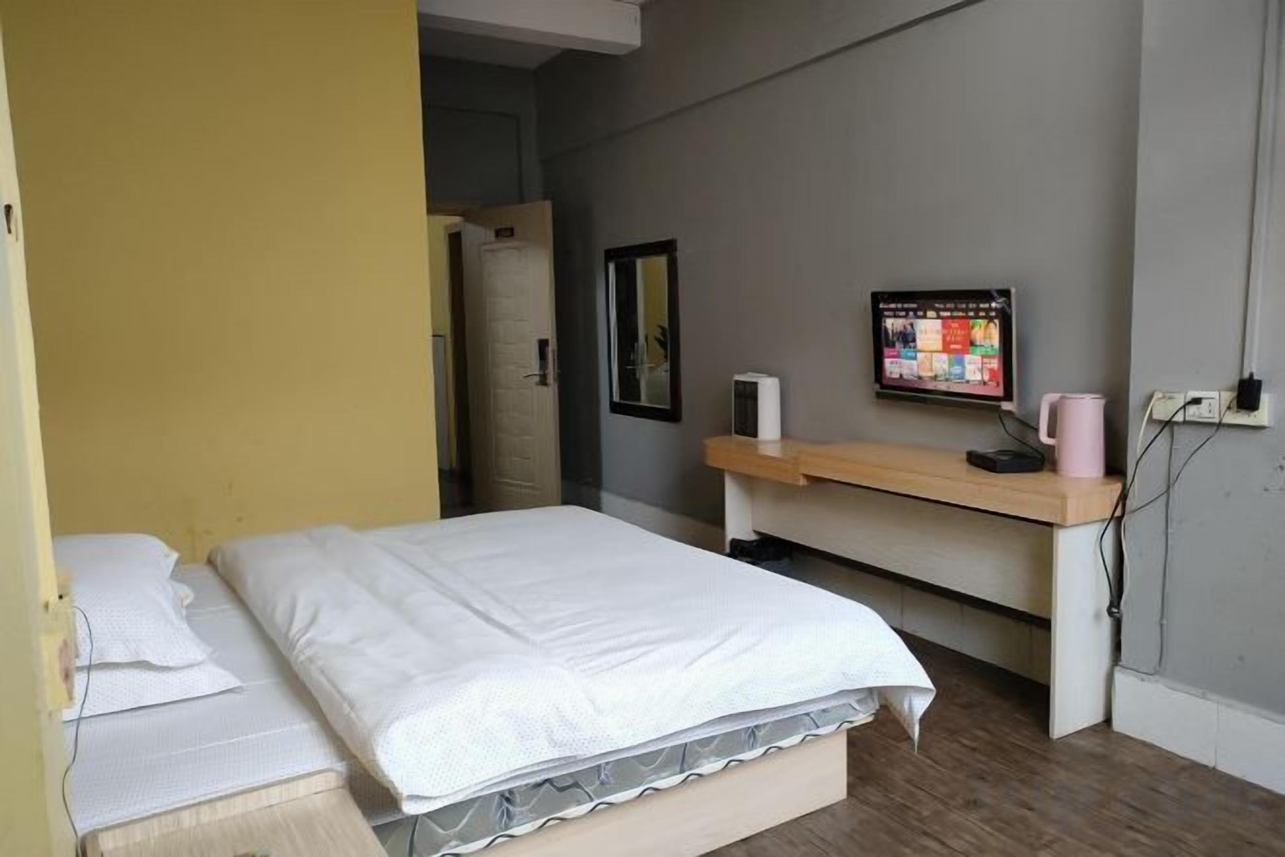 A room with a bed, a desk, a computer monitor, and a wall-mounted mirror.