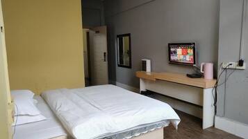 A room with a bed, a desk, a computer monitor, and a wall-mounted mirror.