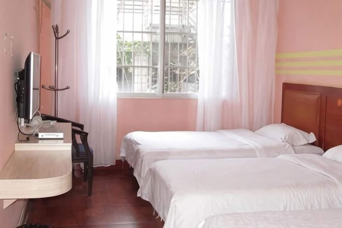 A hotel room with two beds, a desk with a chair, a TV, and a window with curtains.