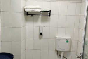 Un baño con inodoro, dispensador de jabón y repisas con toallas dobladas.