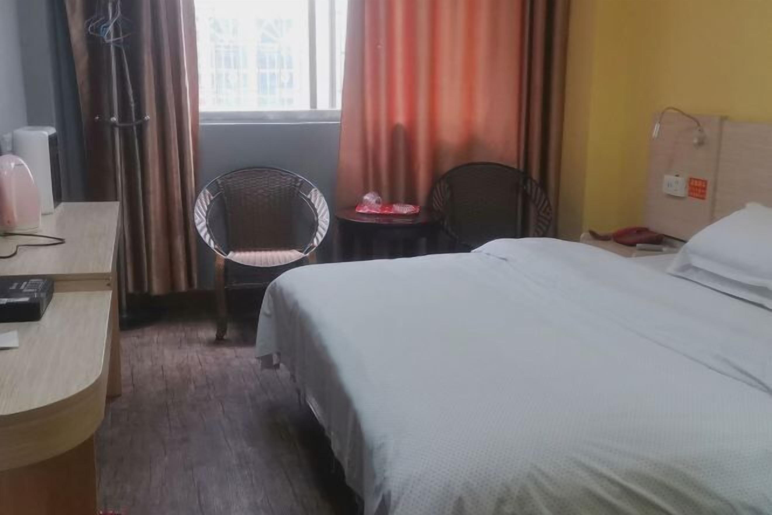 Una habitación de hotel con cama, escritorio, silla y ventana con cortinas.