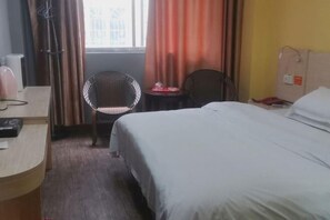 A hotel room with a bed, a desk, a chair, and a window with curtains. - Jinxin Hotel (Hezhou)