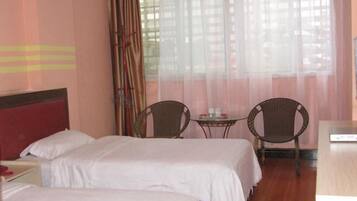 Habitación de hotel con dos camas, una mesita pequeña, dos sillas y un escritorio.