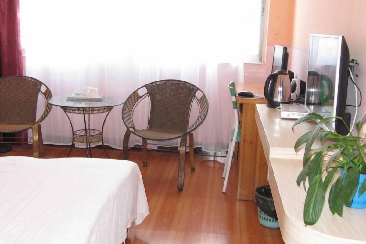 A room with a bed, two wicker chairs, a small round table, a coffee maker, a computer, and a potted plant.