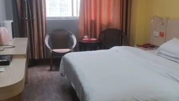 Habitación de hotel con cama, escritorio, silla y ventana con cortinas.