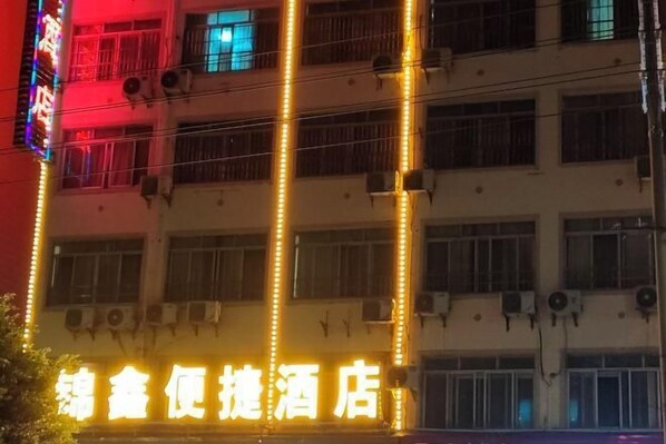 A hotel with multiple floors, air conditioning units, and a brightly lit sign with Chinese characters.