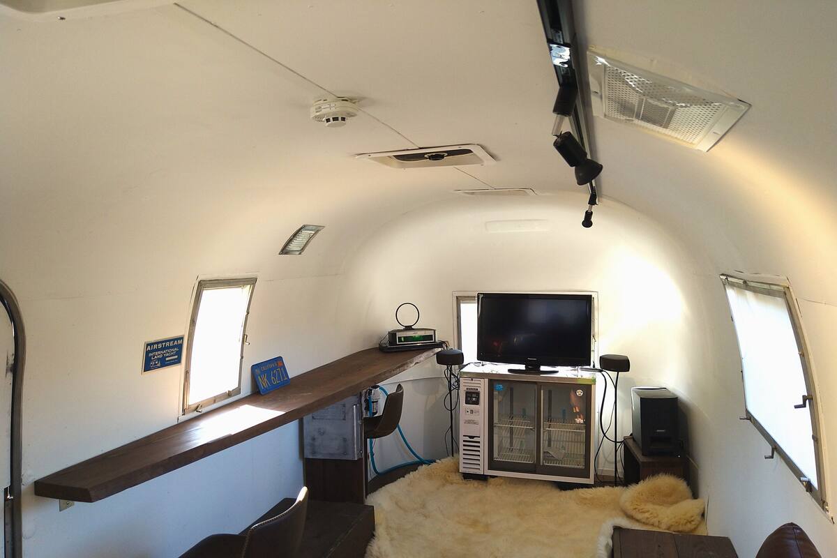 A compact RV interior with a television, a small kitchenette, a fur rug, and a wooden shelf.