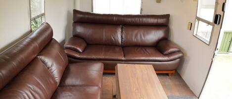 A compact RV interior with a brown leather sofa, a wooden table, and a small window.