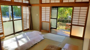 A traditional Japanese room with tatami flooring, a bed with white bedding, sliding shoji doors, and a view of a garden. - SEA-DWELLER Inn (Miyazaki)