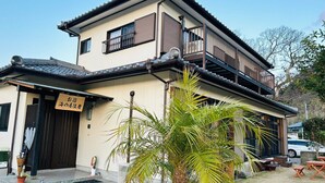 A traditional Japanese-style building with a two-story structure, a balcony, and a small garden area with a palm tree. - SEA-DWELLER Inn (Miyazaki)