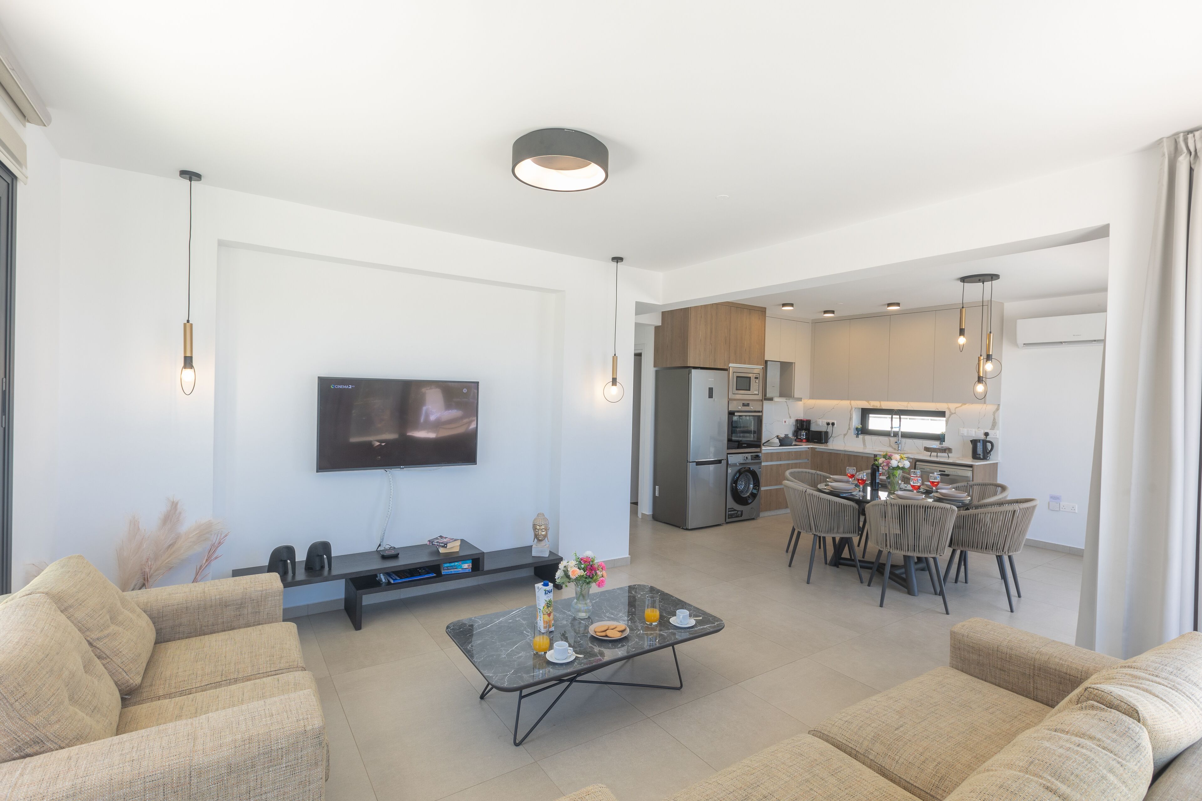 Una sala de estar moderna con un televisor de pantalla plana, una mesa de centro con alimentos para el desayuno, un sofá y una zona de comedor con sillas y una mesa.