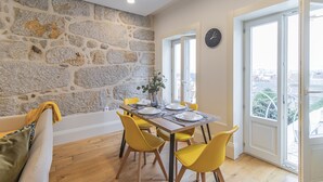 Un coin repas avec un mur en pierre, un plancher en bois, des chaises jaunes et une table dressée pour quatre personnes.