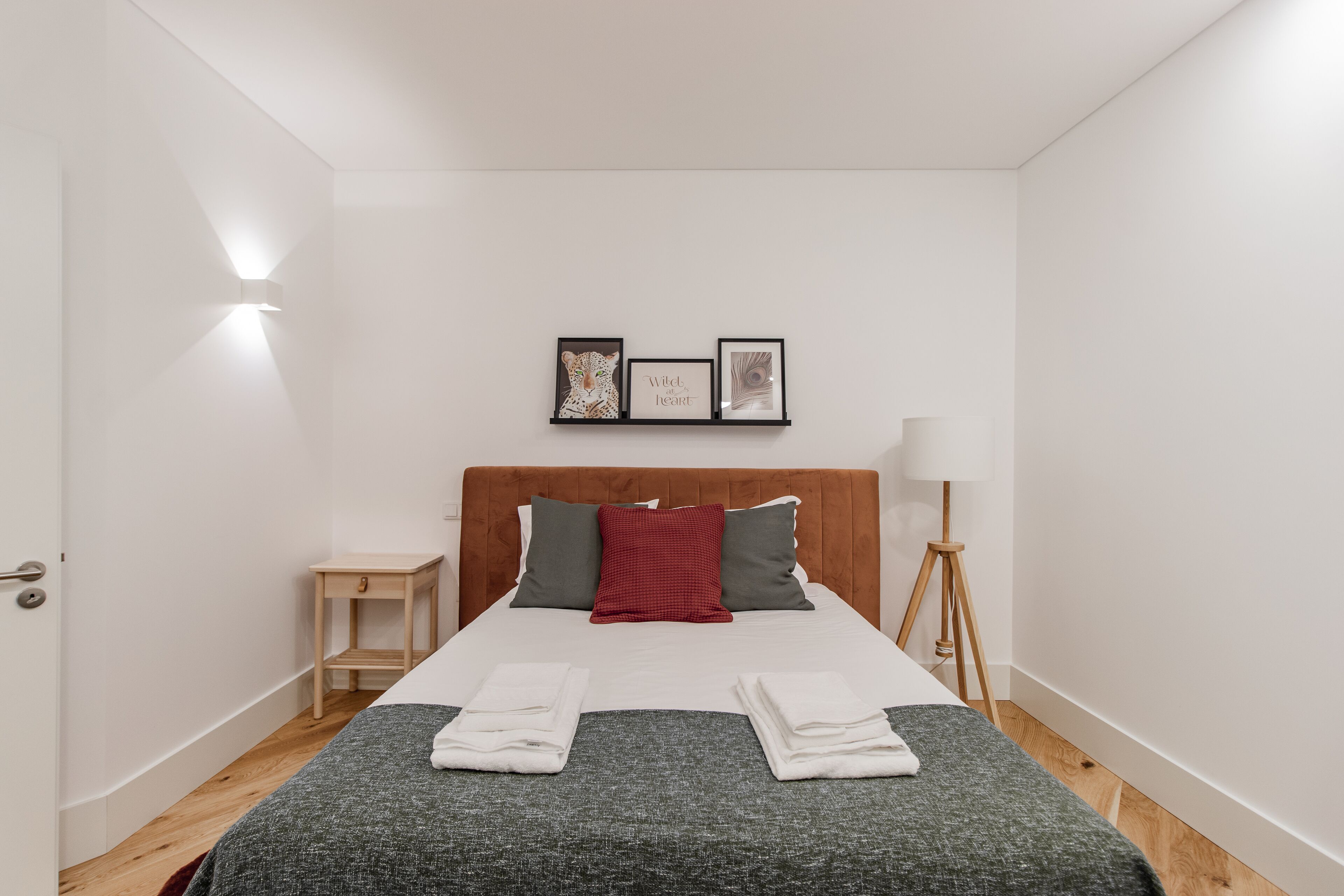A hotel room with a bed, a bedside table, a lamp, and wall art.