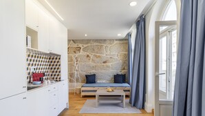 Une cuisine moderne avec des meubles blancs, un mur en pierre, un banc en bois et une table à manger sur laquelle se trouve un saladier rempli de fruits.