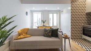 Un salon moderne avec un canapé, une petite table sur laquelle se trouve un verre de jus de fruits, et un coin cuisine doté d’un crédence décorée.