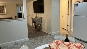 A modern kitchen with a refrigerator, a dining table, and a TV mounted on the wall.