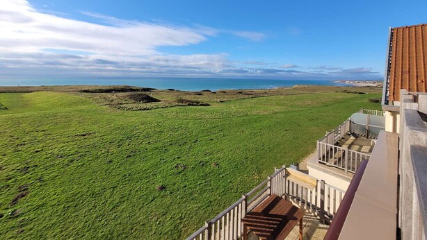 Vista costera desde un balcón, con un campo de césped y el mar al fondo.
