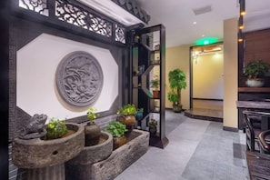 A reception area with a decorative wall, a reception desk, and potted plants. - Qingyi Holiday Hostel (Hangzhou)