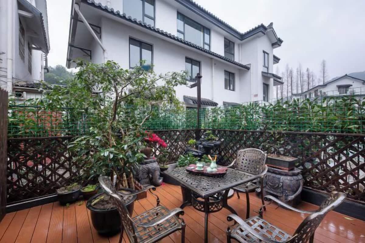 A wooden deck with a table and chairs, surrounded by potted plants and a decorative fence.
