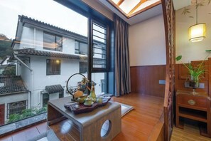 A traditional Japanese-style room with tatami flooring, a low wooden table with a tray of tea and utensils, and a view of a neighboring building through large windows. - Qingyi Holiday Hostel (Hangzhou)