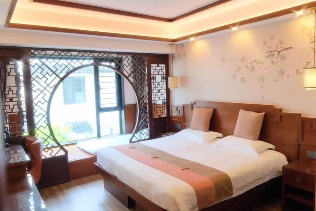 A hotel room with a large bed, a desk, and a view through a decorative window.