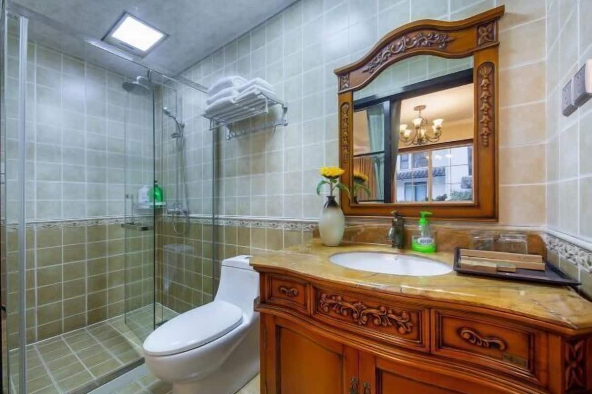 A bathroom with a glass-enclosed shower, a white toilet, a wooden vanity with a mirror, and a vase with a yellow flower.